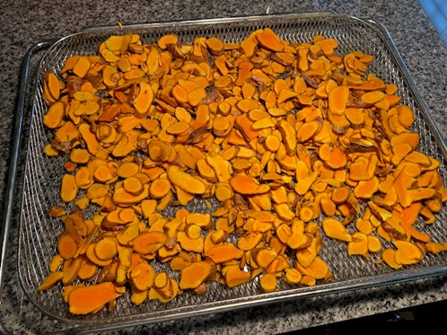 Thin slices of golden turmeric spread on a silver drying rack