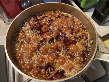 sour cherries, ginger, hibiscus flowers, orange peel and rosemary boiling in a sauce pan on a stove