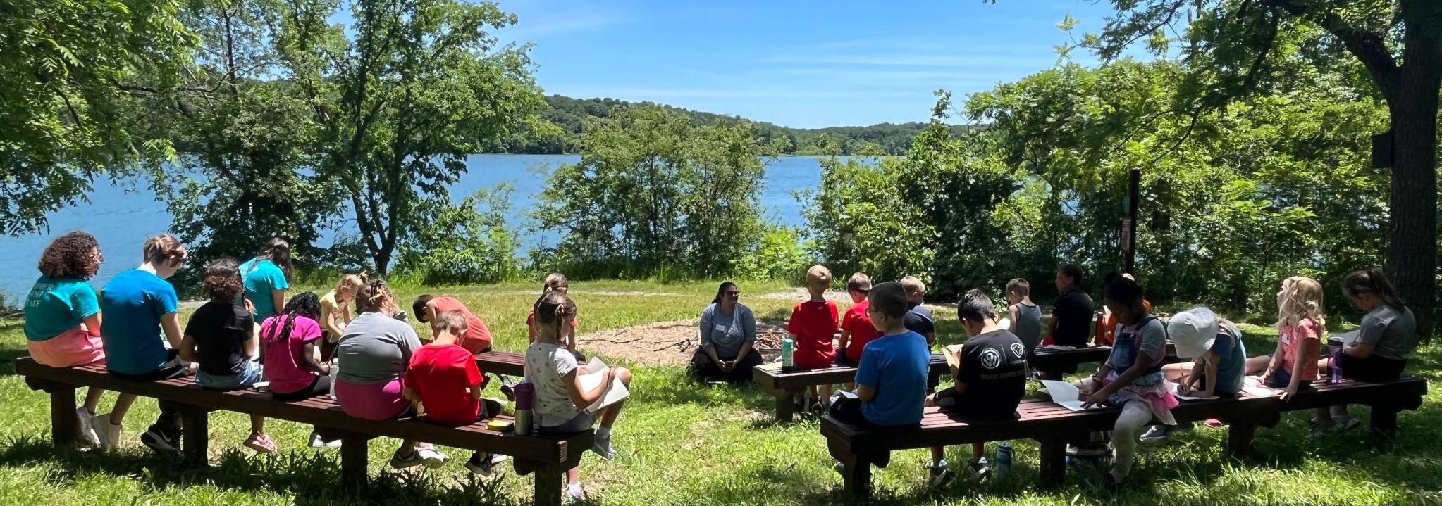 children sitting on wood benches outside in front of the lake at Mr. and Mrs. F. L. Schlagle library