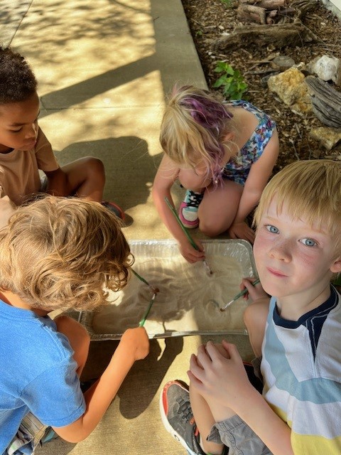 group of children surrounding a flat container brushing away sand to look for fossils