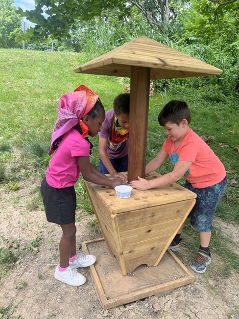3 children playing around an outdoor wooden table with cover