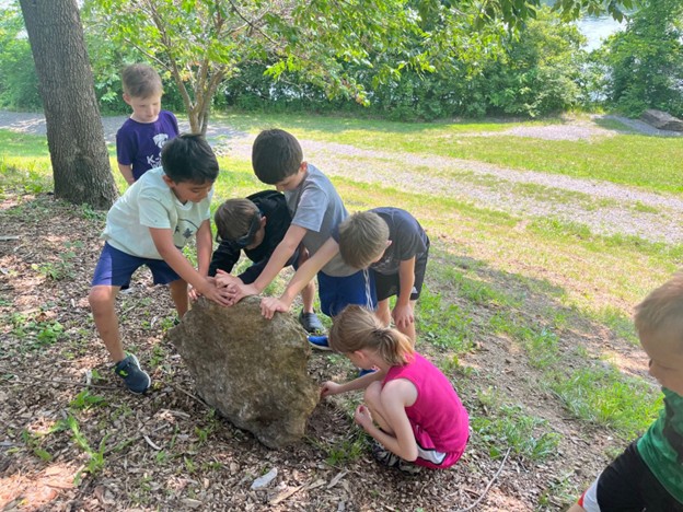 children looking under a large rock outside