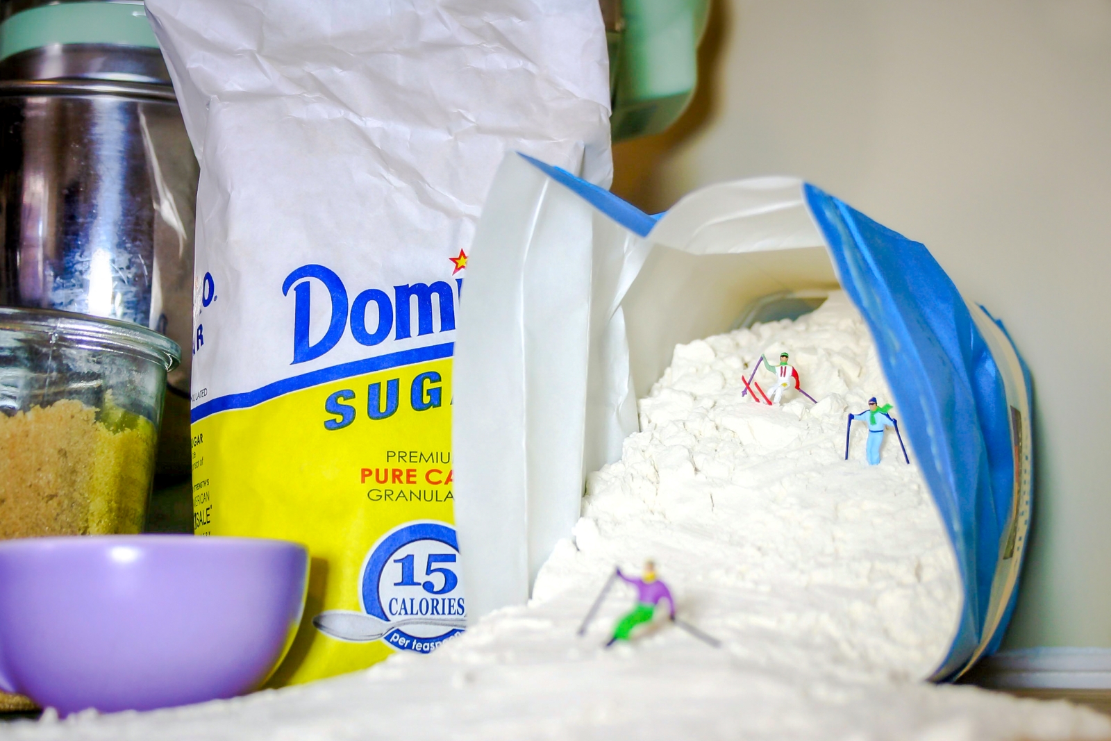 a bag of flour poured out on its side with miniature people figurines skiing down the flour.