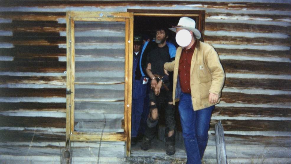 Arrest of Theodore Kaczynski, the Unabomber, by FBI agents at his cabin in Montana, 1996. He is being led out of the front door in handcuffs by an agent whose face is censored.