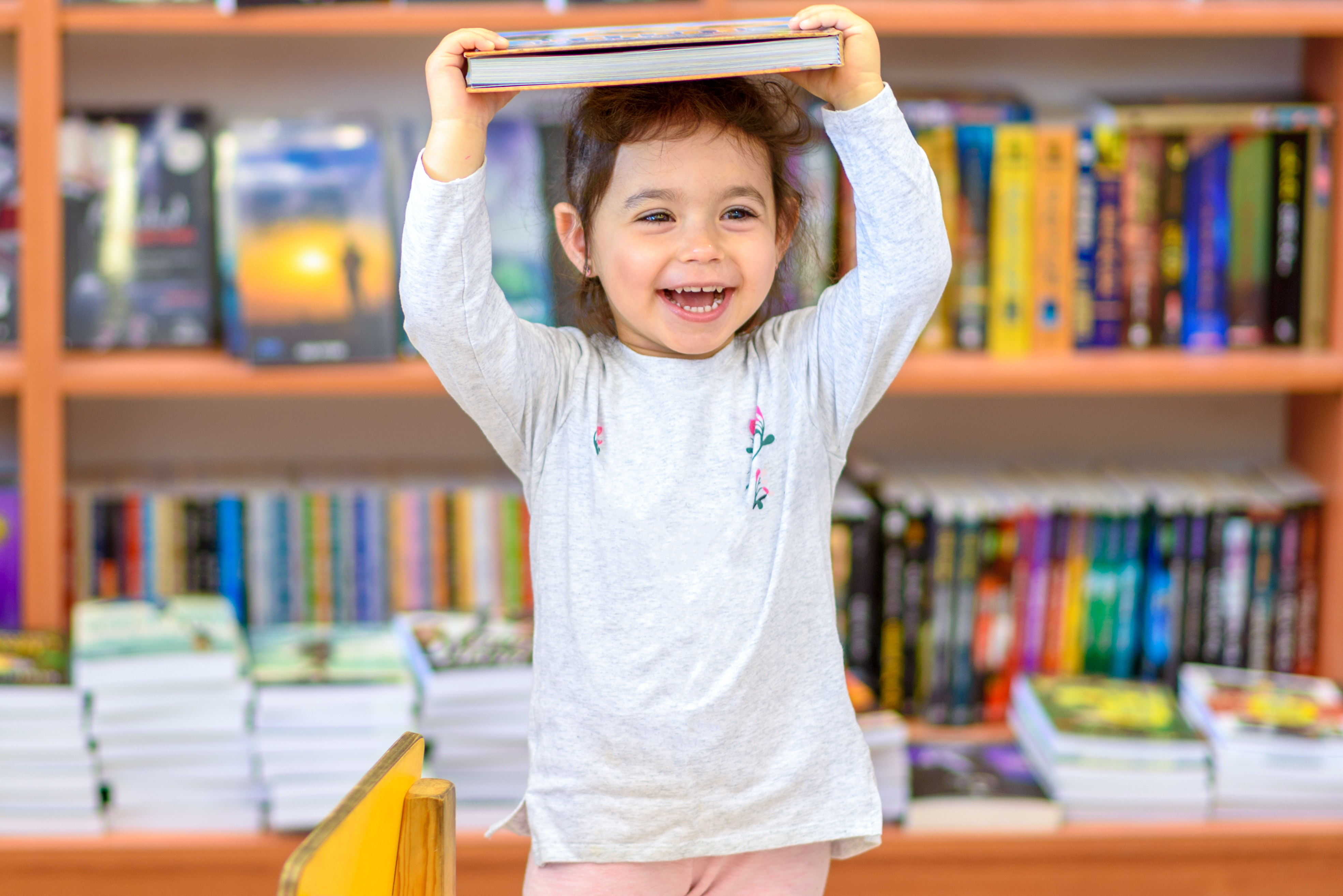 toddler holding a book over here head inside a library