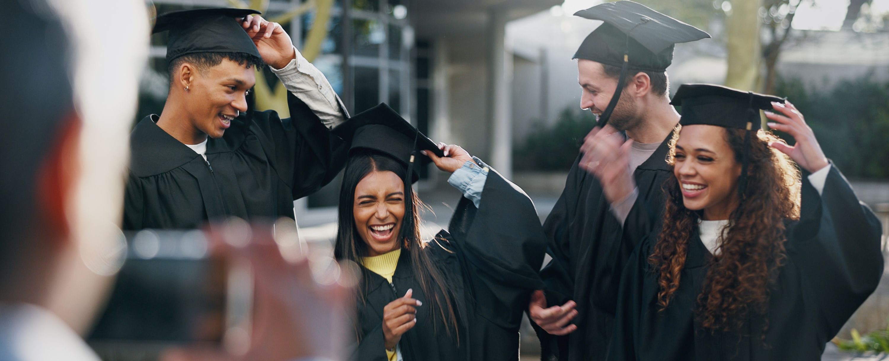 group of 4 students in black graduation cap and gowns getting ready to have their picture taken