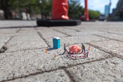 miniature people figurines on a brick sidewalk using construction equipment to remove a piece of bubble gum, image by Luke Pech