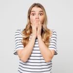 shocked woman in striped shirt with hands covering mouth