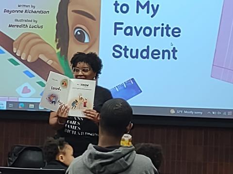 Dayonne Richardson holding a book reading to an audience.