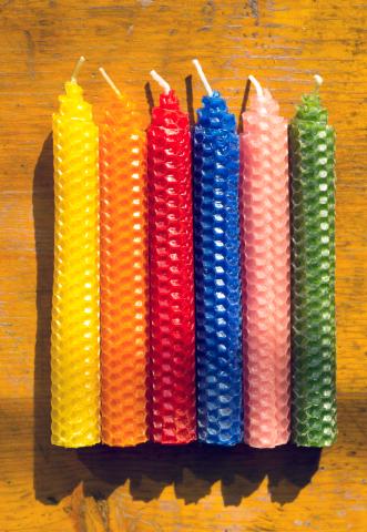 various colors of taper candles made from rolled beeswax sheets, laying on a wooden surface