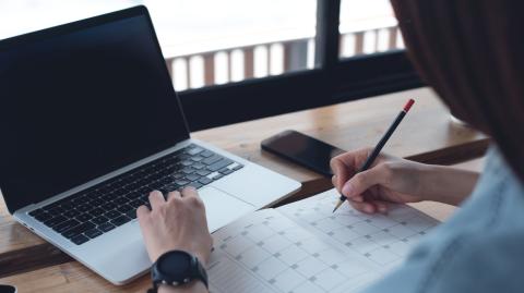 woman writing in notebook in front of computer