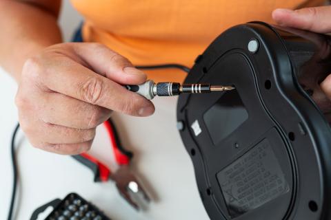 A person with dry skin repairs a broken appliance using a small screwdriver
