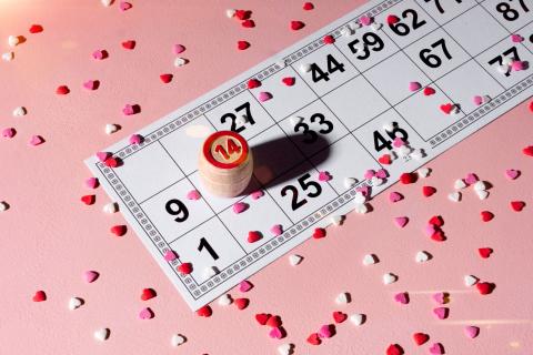bingo board and marker on a pink surface with valentines heart confetti