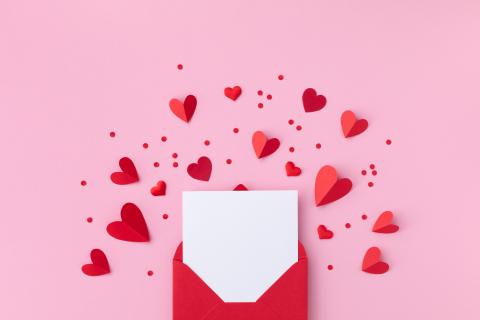 Flat lay with pink background red envelope, paper card and various red paper hearts 
