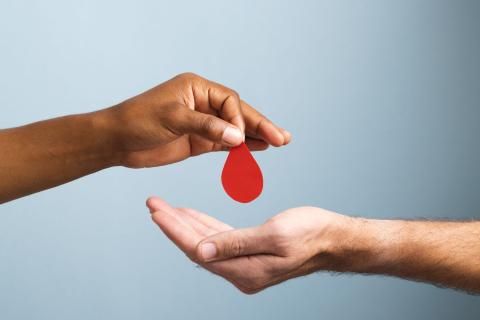 a persons hand placing a red paper shaped like a large droplet into another persons hand