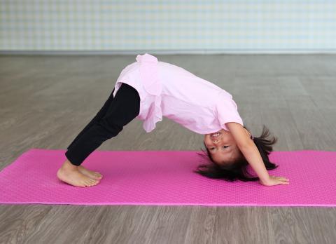 young girl in pink leotard doing yoga on a pink mat