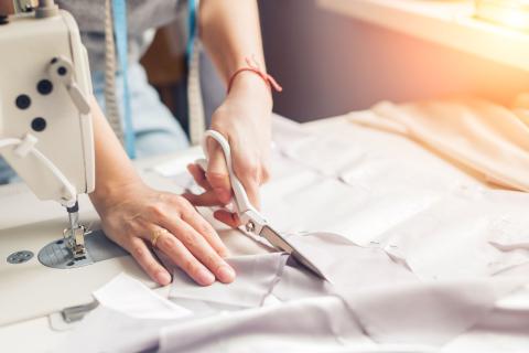 person cutting fabric next to a sewing machine