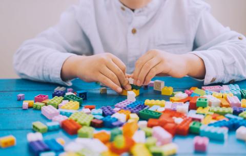 young person sitting playing with Lego bricks that are spread out on a table