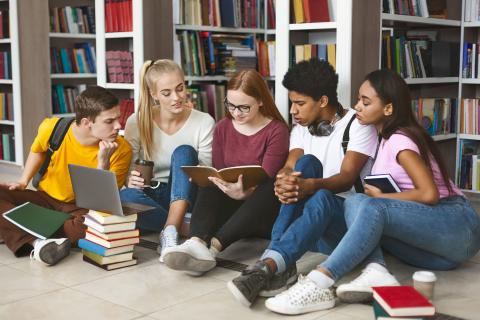 group of teenagers sitting on the floor of a library looking at materials