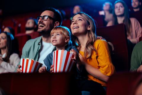 small child sits between a man and woman in a movie theater eating popcorn