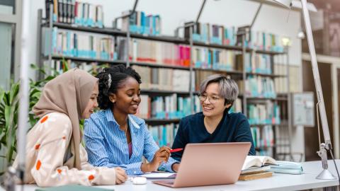 3 women sitting at a table in a library talking