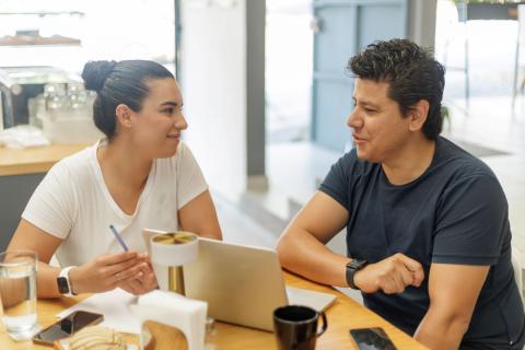 Hispanic couple sits at a table talking in a cafe