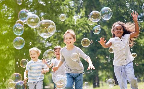 a group of children running through a field chasing bubbles