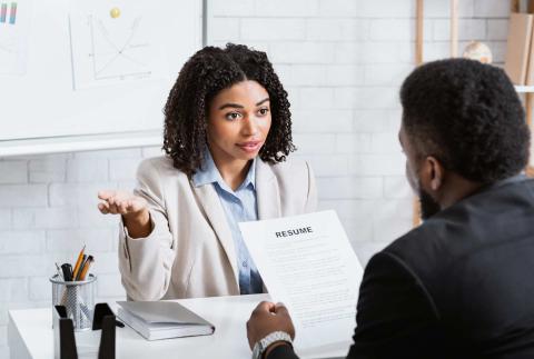 A professional looking man and woman sit at a desk discussing a resume. 