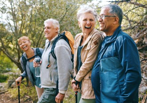 Four older adults laugh with one another while hiking. 