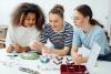 Three young women sitting together at a table making jewelry.