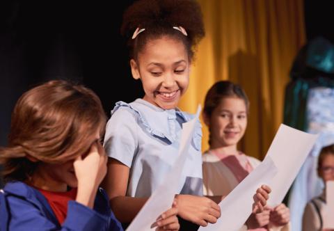 children on stage at a theater reading from scripts