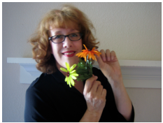 Jo Ho, storyteller (red hair, black glasses, black blouse) holding a yellow daisy and an orange daisy, smiling
