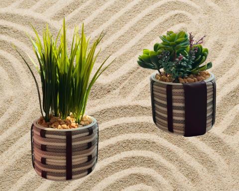 Two cord-wrapped planters with fake succulent plants. The cords are three neutral light shades. The planters are adorned with leather strips, woven into the cord design. The plants are held in place with brown pebbles. They are floating over a raked sand background.