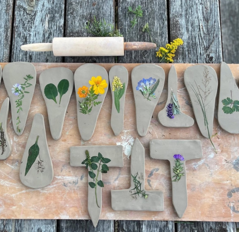flattened clay works with flowers and plants inside, laying on a wooden table, below a rolling pin