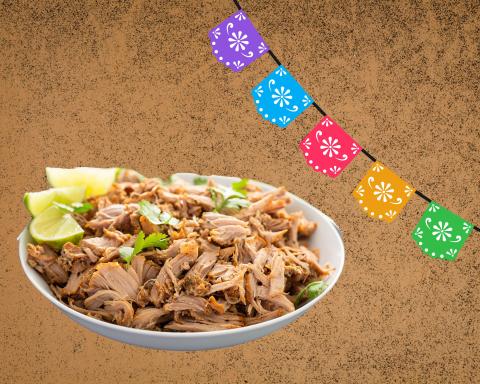 A brown rustic background shows multi-colored tissue flags that have different punched patterns and then there is a white bowl with shredded pork fried up with a side of cut limes. 
