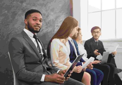 A diverse group of professional young people are seated, holding items like resumes and personal devices.