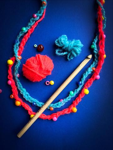 Red and Blue Crochet necklace with the balls of colored yarn next to them on a dark blue background
