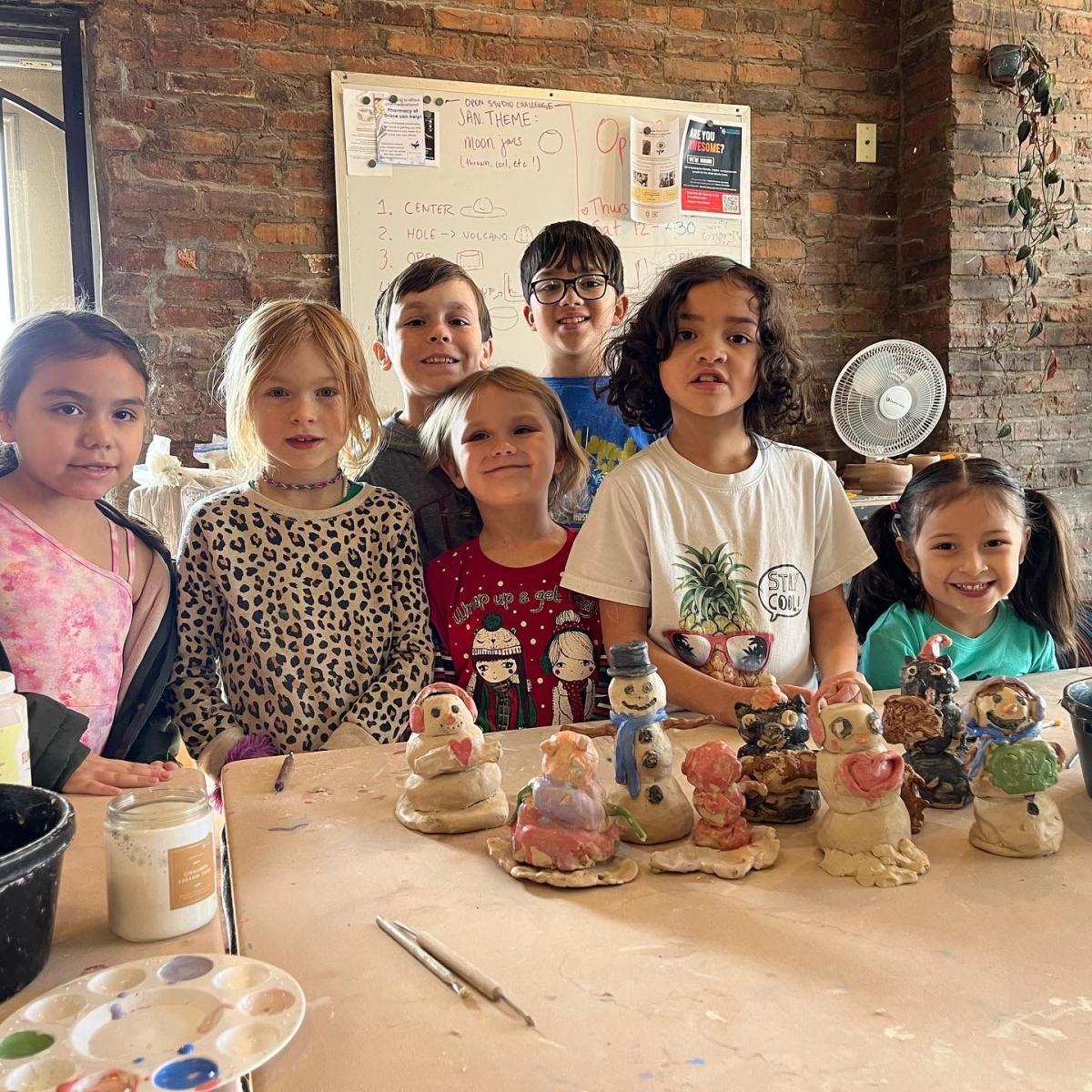 7 children standing around clay pieces.