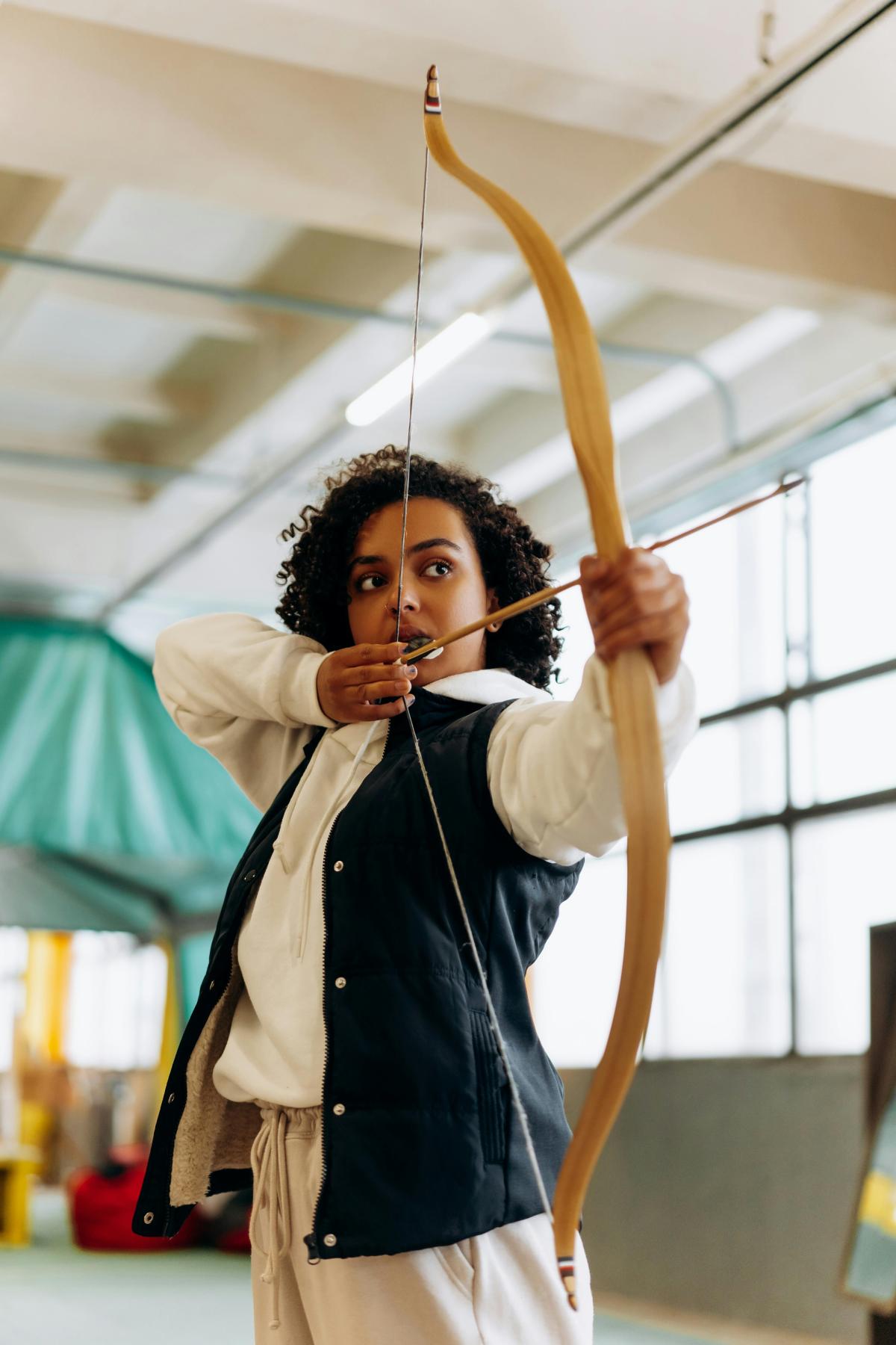 A girl holding a bow indoors in archer stance