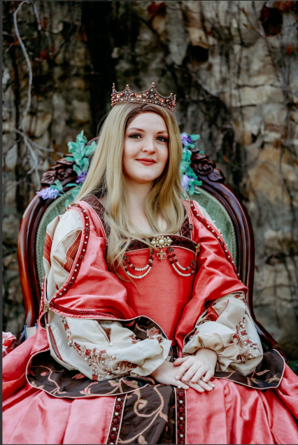 Princess Gwenevere sitting in a chair; pink flowing dress; wearing a crown