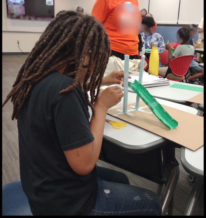 Student with long braids creating a roller coaster slide from a standing post.
