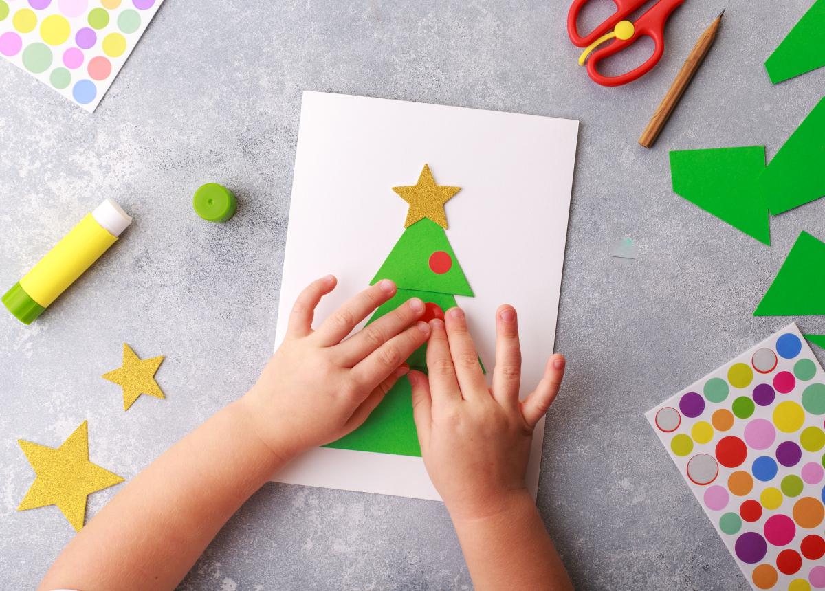 Child's hands decorating a card with a Christmas tree