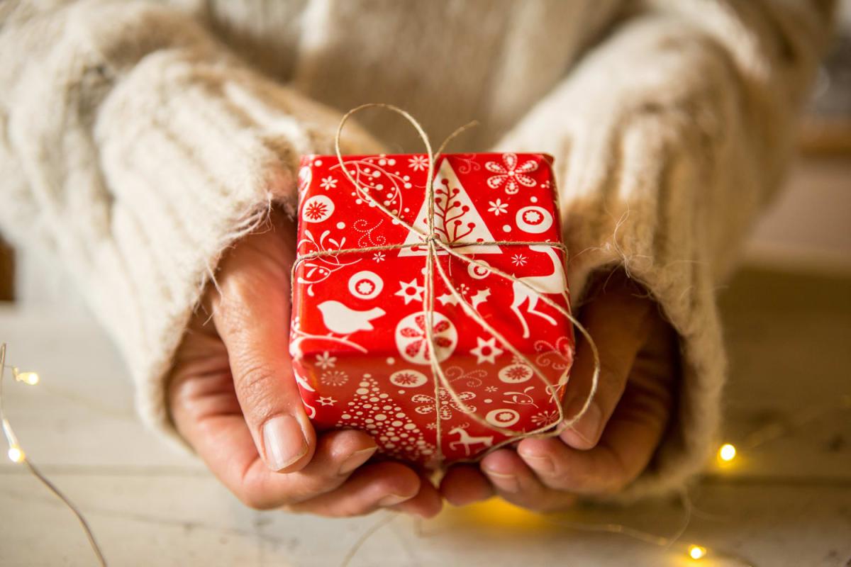 Hands holding a small wrapped red gift. Manos agarrando un regalo envuelto pequeño y rojo.