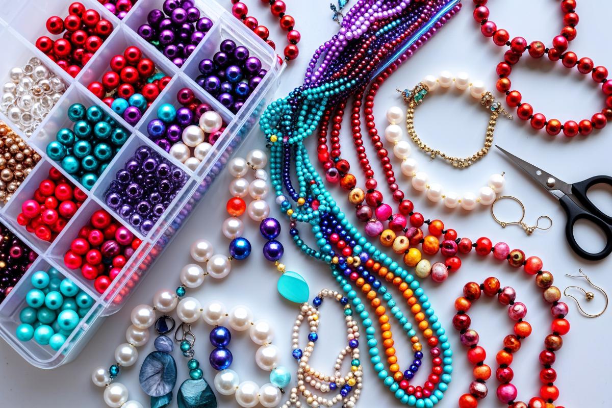 Strings of colorful beads and a pair of scissors on a white background next to a box of loose beads