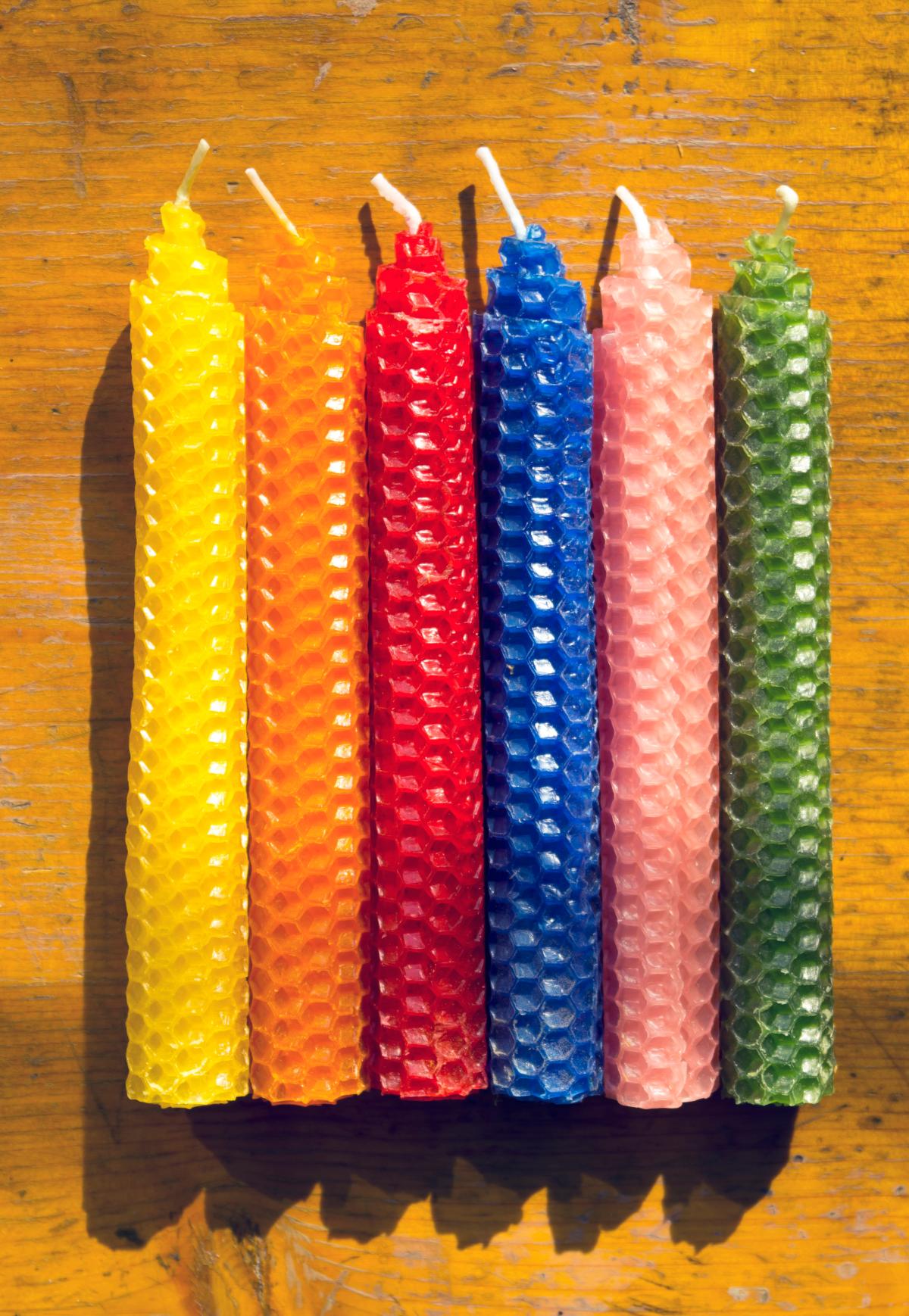 various colors of taper candles made from rolled beeswax sheets, laying on a wooden surface