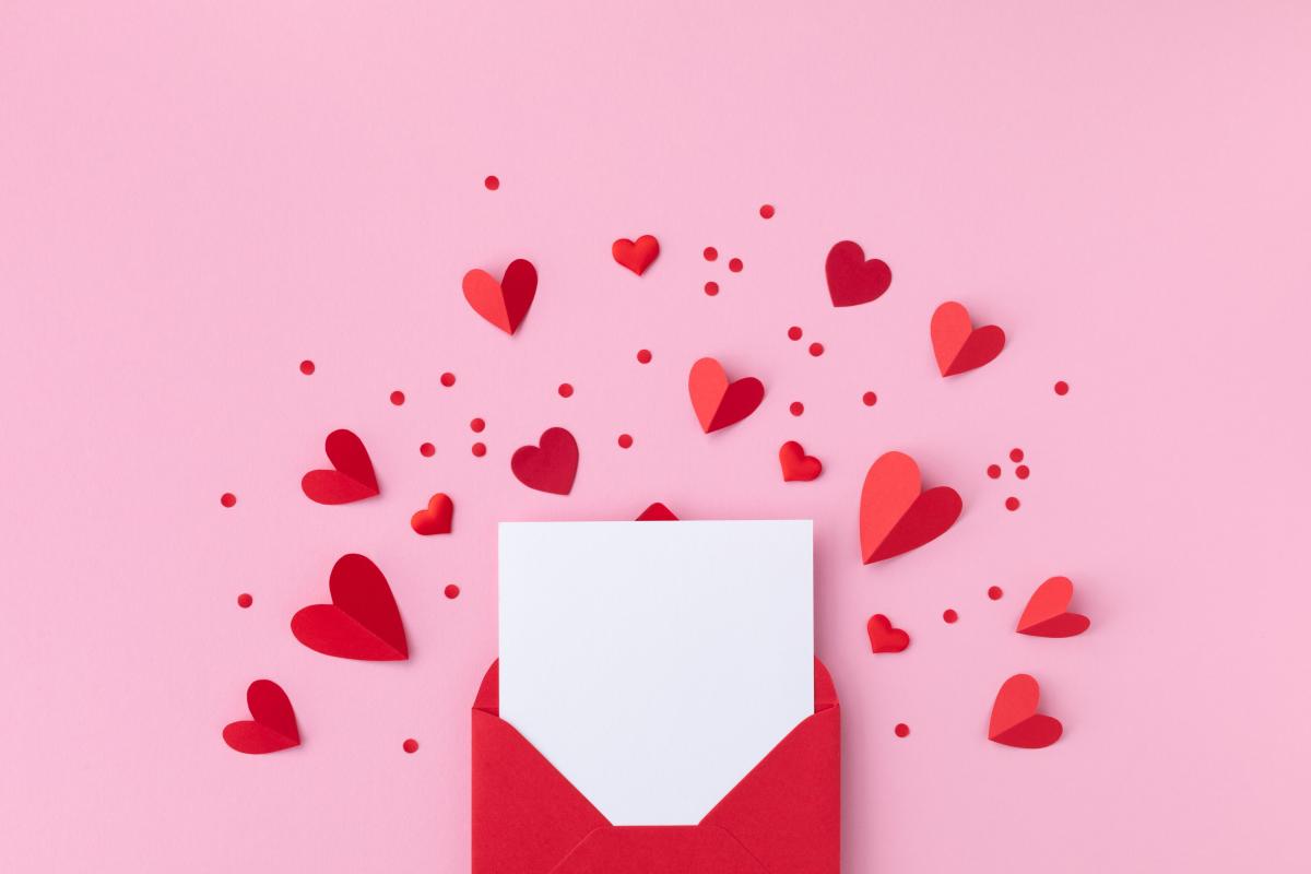 Flat lay with pink background red envelope, paper card and various red paper hearts 