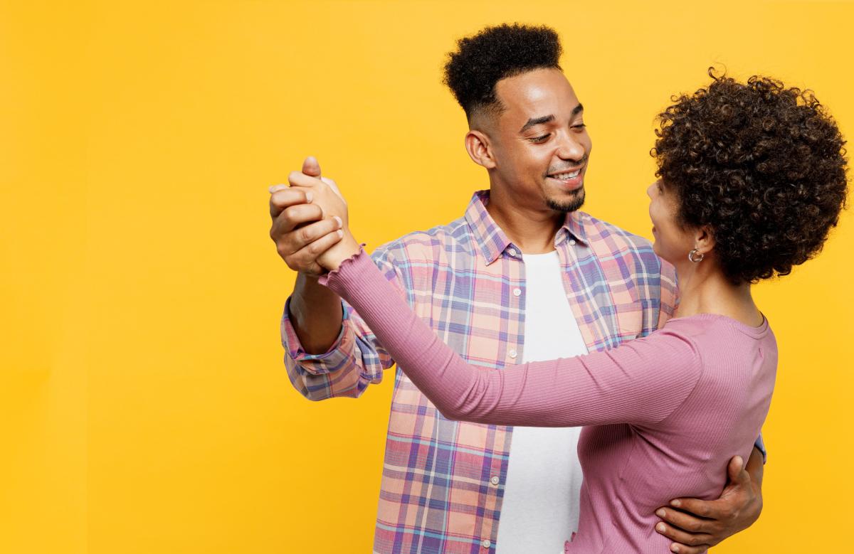 Couple dancing in front of a yellow background. 