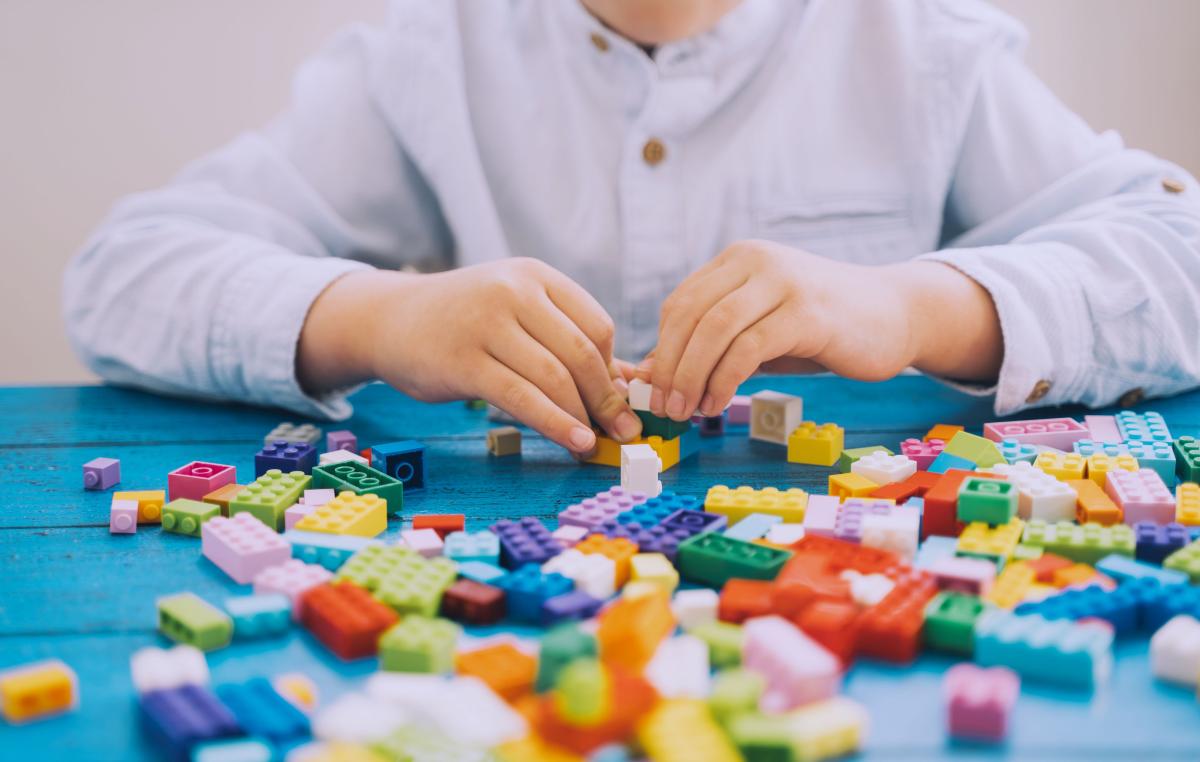 young person sitting playing with Lego bricks that are spread out on a table