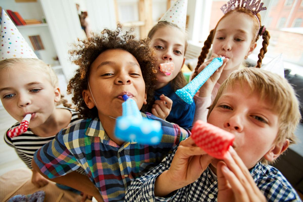 High angle view at multi ethnic group of children blowing party horns at camera