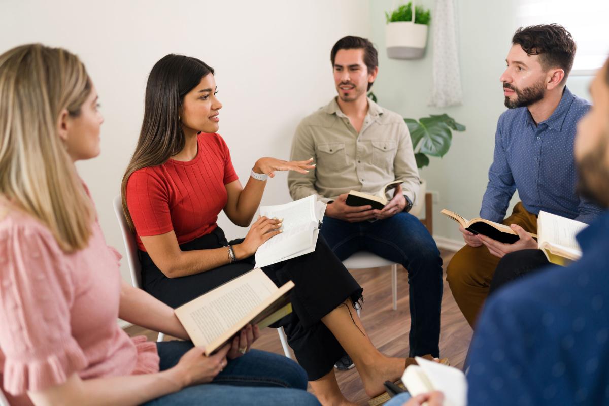 group of happy people sitting with open books on their laps talking to each other